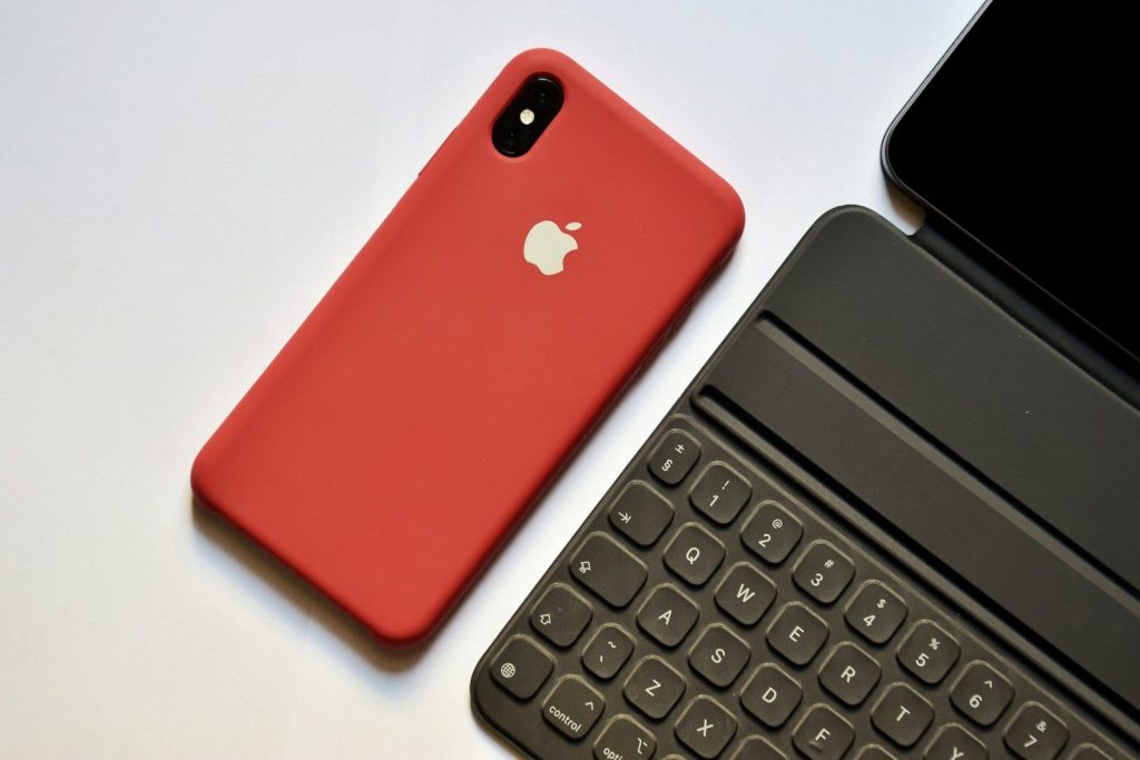 space gray iPhone with red case beside tablet keyboard