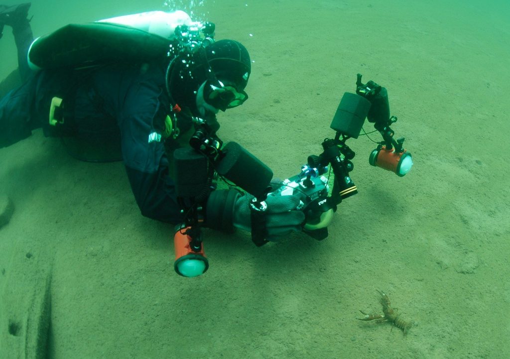 A scuba diver films underwater with specialized equipment.