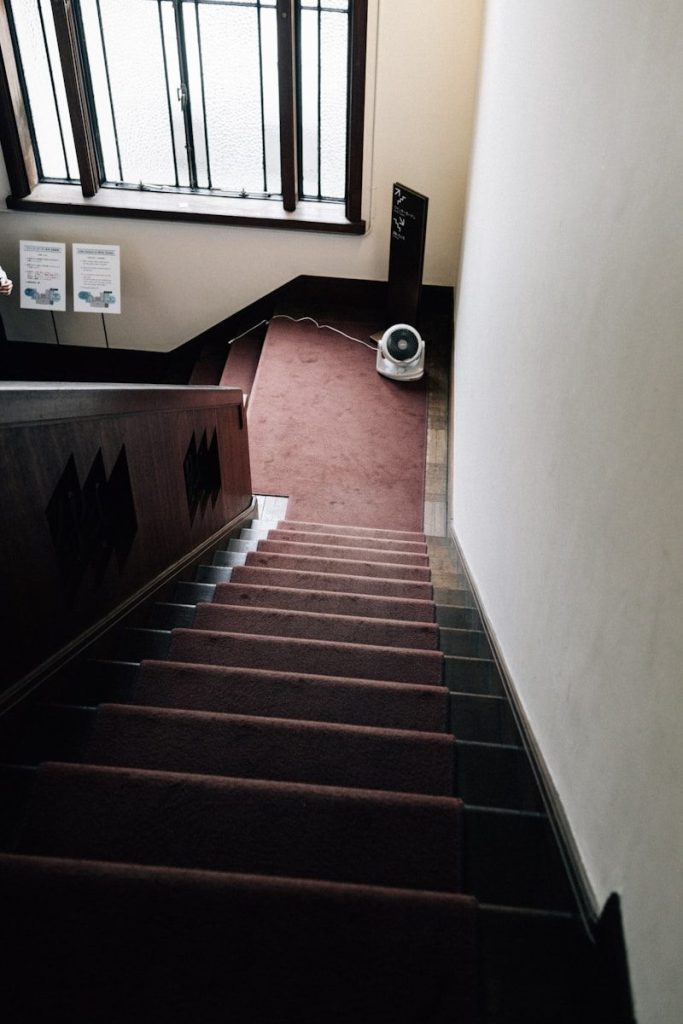 Carpeted staircase with wooden banister and window.