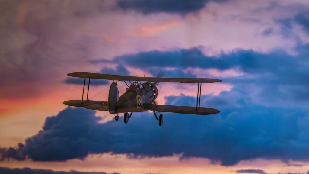 Biplane flying through dramatic clouds at sunset