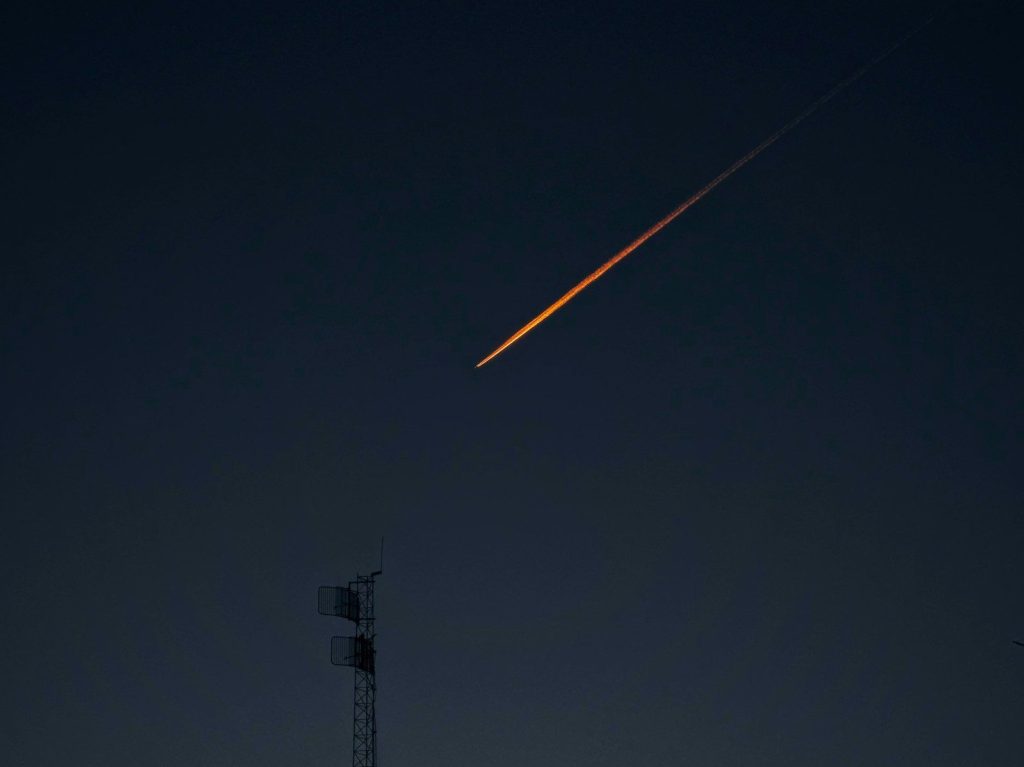 An airplane contrail glows orange against a dark sky.