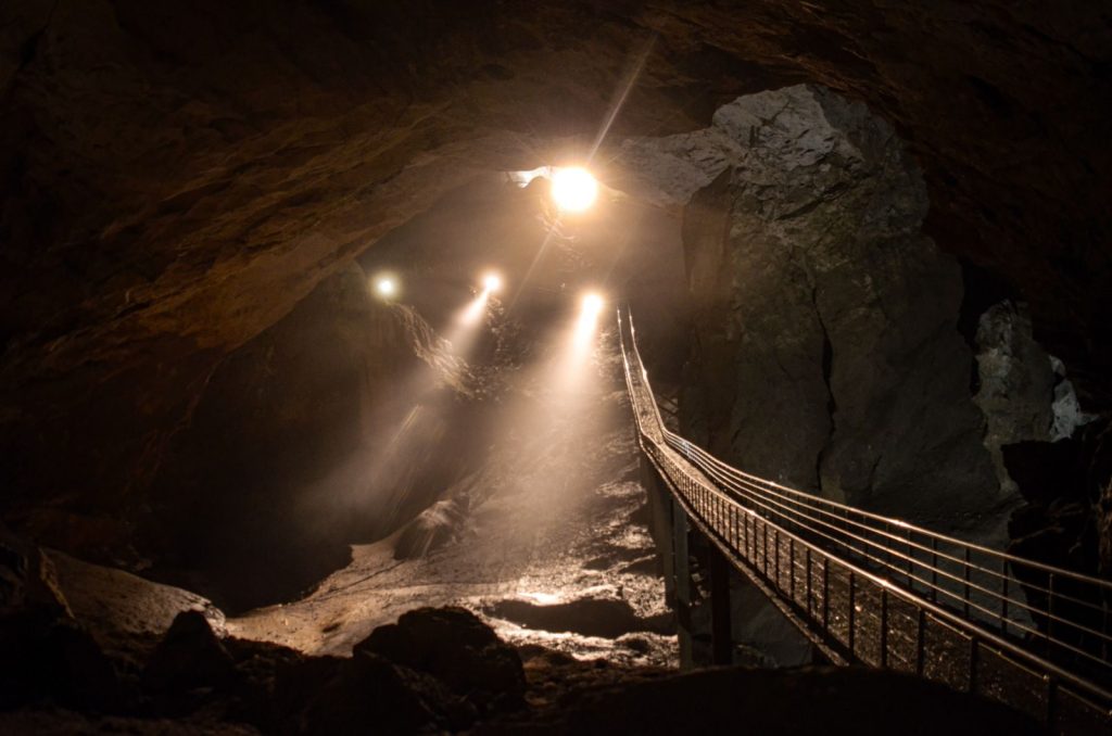 A dramatic view of sunlight illuminating a cave with a wooden bridge. Captivating geological wonder.