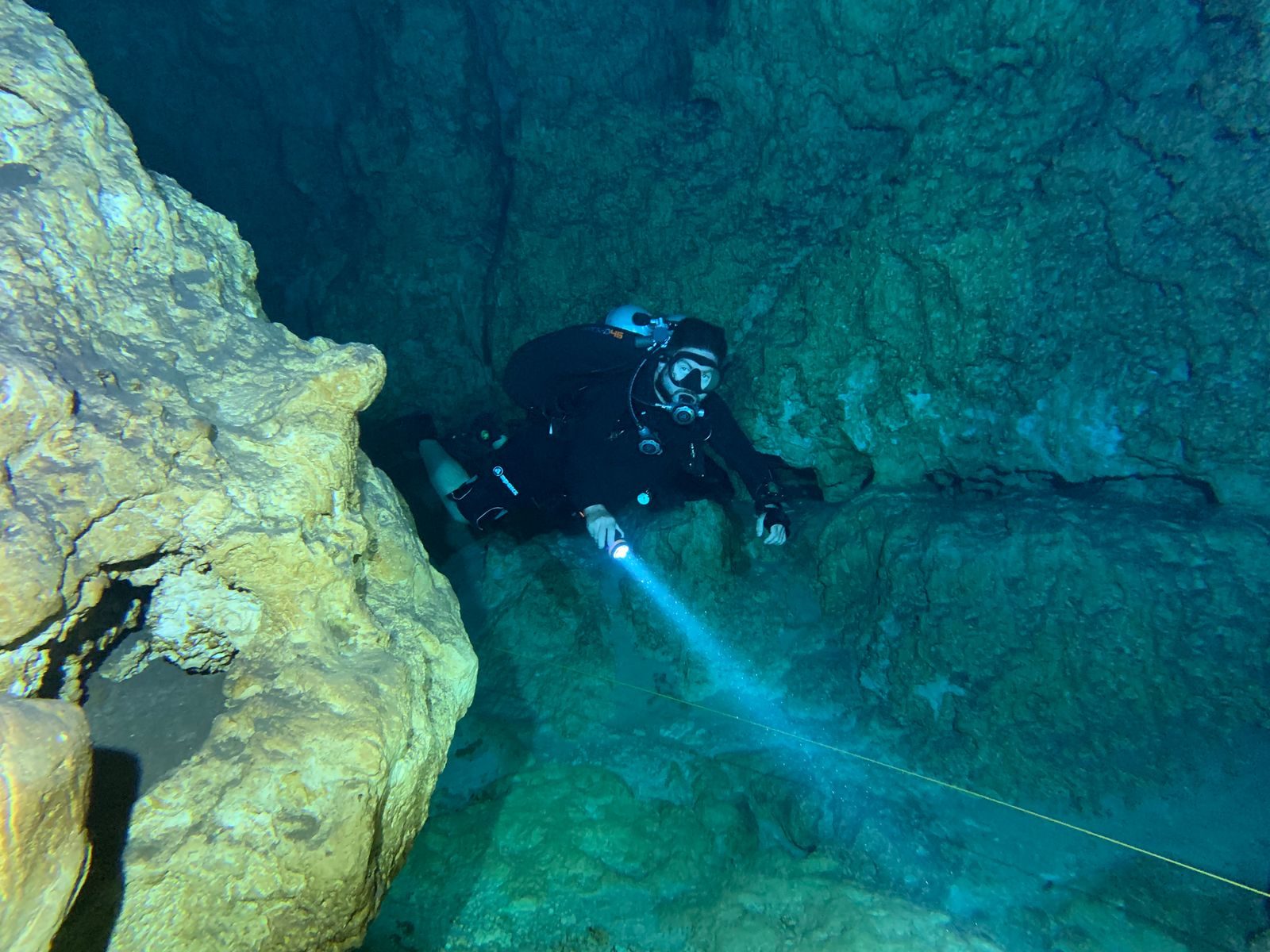 A scuba diver explores the depths of an underwater cave with a flashlight.
