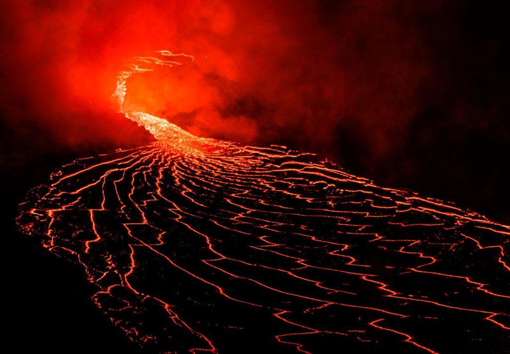 Spectacular lava flow from an erupting volcano under the night sky, showcasing fiery reds and intense heat.