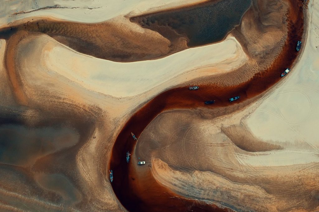 Stunning aerial view of winding river and boats in desert-like terrain, highlighting natural patterns.