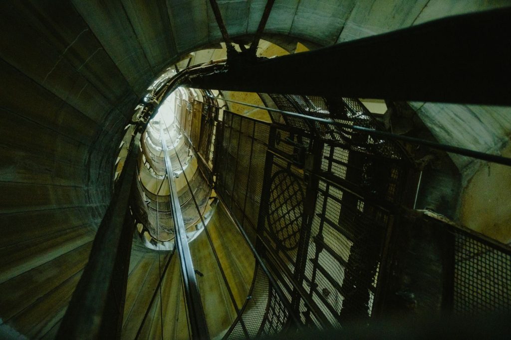 A striking view looking up a spiral elevator shaft with metal structures and wires.