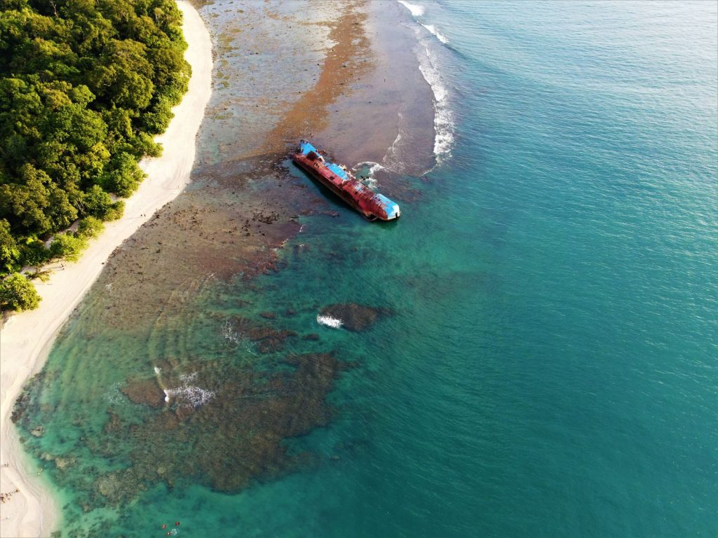 Dramatic aerial shot of a shipwreck near Pangandaran's lush coastline in Indonesia.
