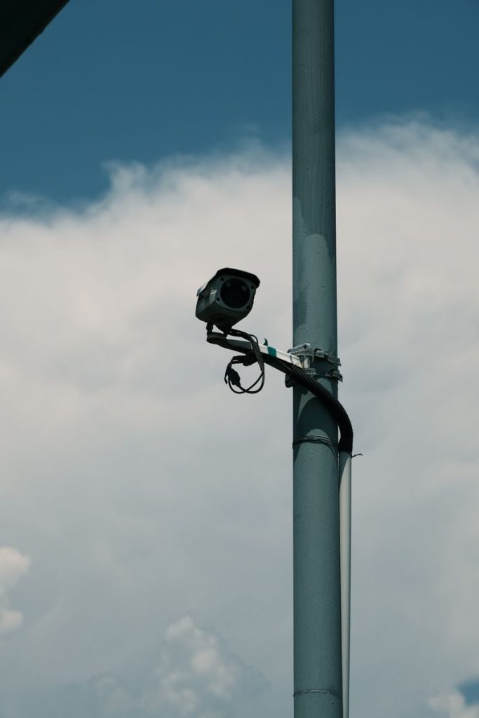 A surveillance camera mounted on a metal pole against a cloudy sky captures outdoor security technology.