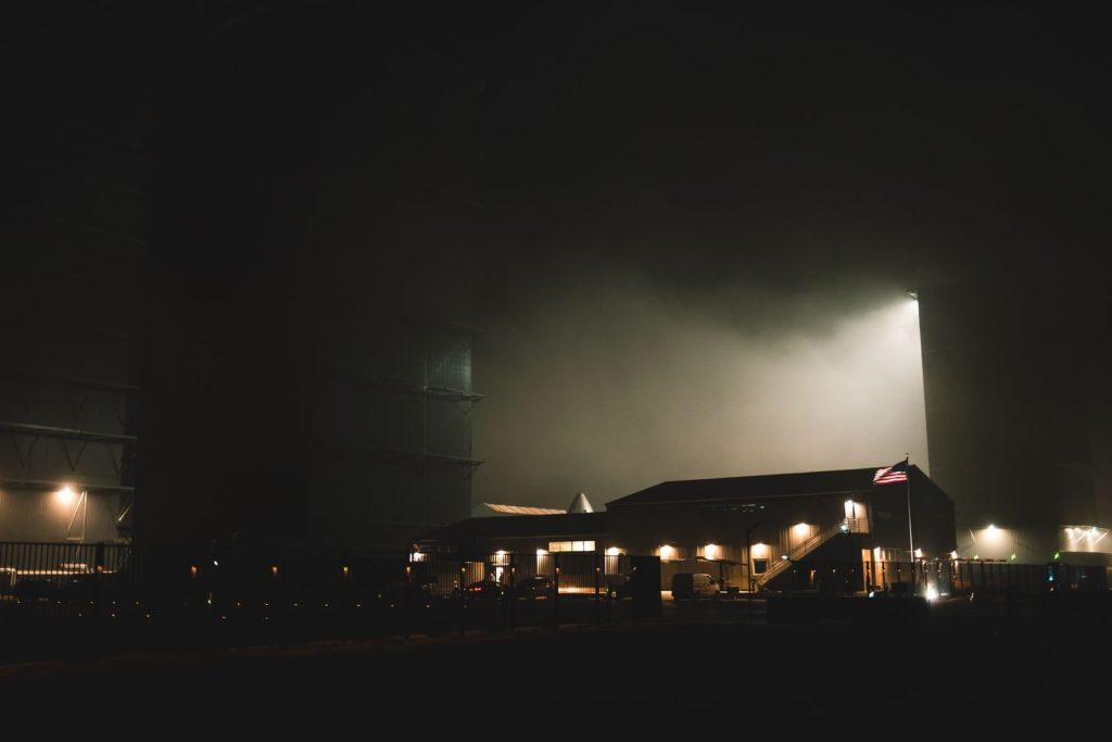 A dramatic nighttime view of an industrial facility at a space exploration center with atmospheric lighting.