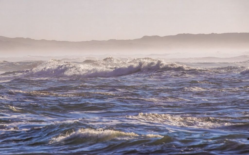 Captivating ocean waves crash against the shore under a soft morning light, creating a serene view.