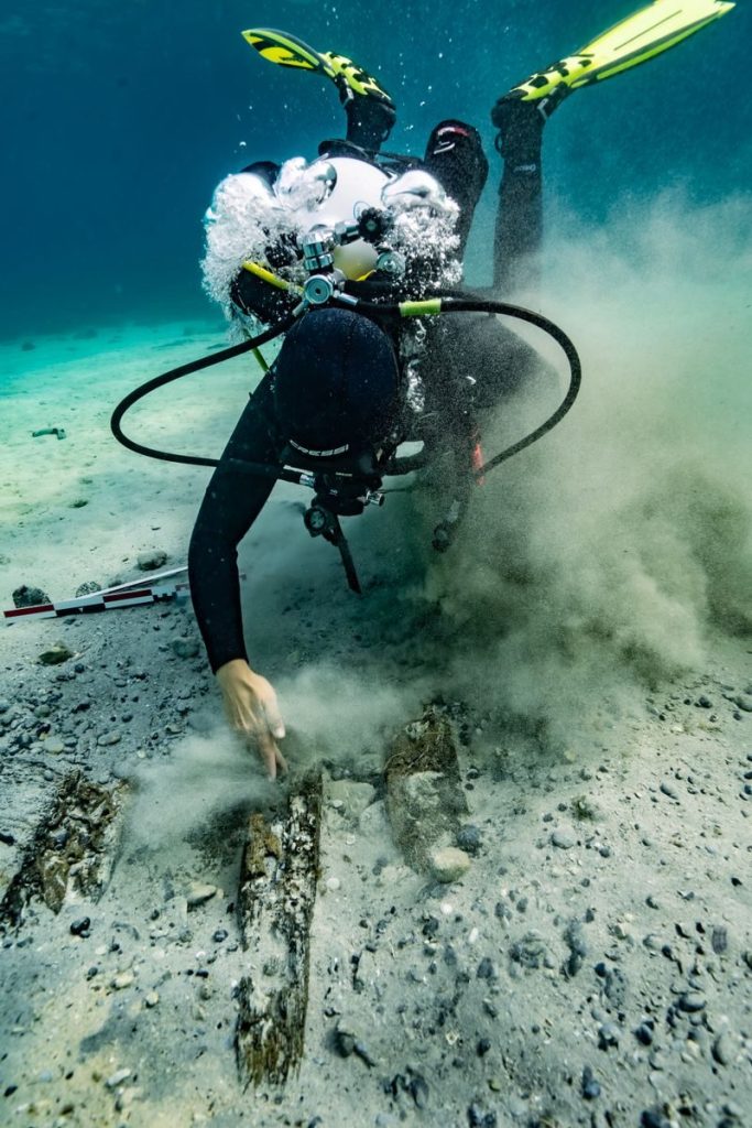 A scuba diver inspects the seabed underwater in Croatia, surrounded by bubbles and sand.