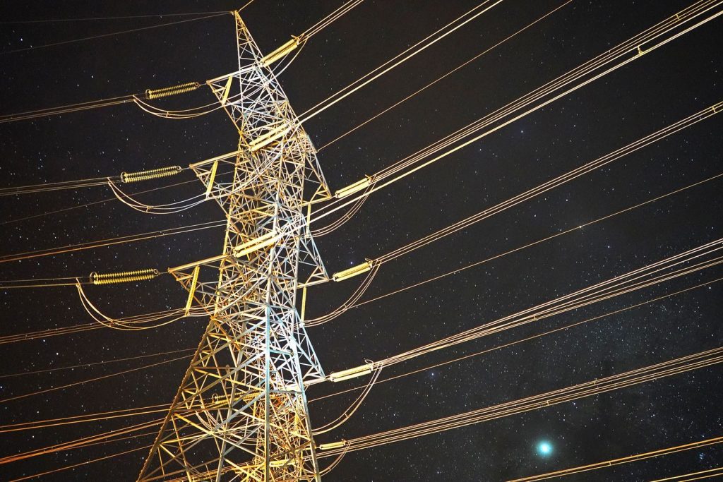 Illuminated power tower against a starry night sky, showcasing energy infrastructure.