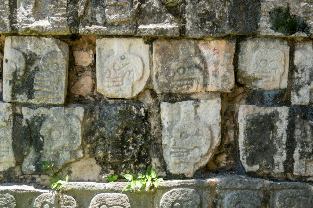 Detailed close-up of ancient Mayan stone wall with carved skulls at Chichén Itzá, Mexico.