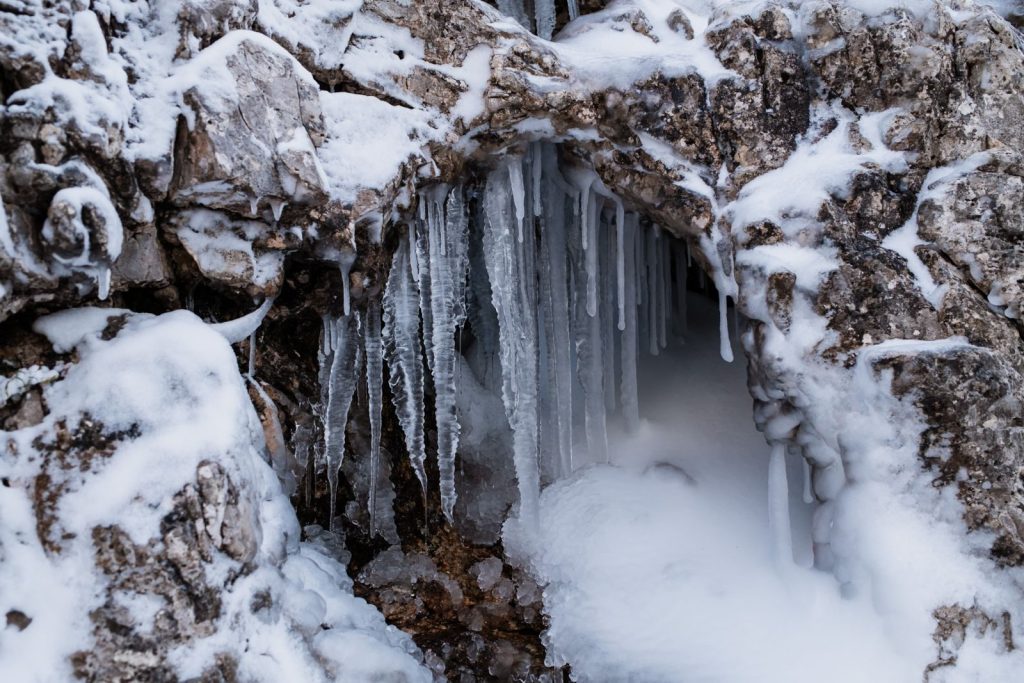 Close-up of icicles forming on a snow-covered rocky arch, showcasing winter's cold beauty.