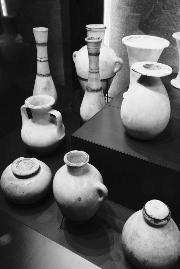 A display of ancient ceramic vessels in a museum setting, captured in black and white.