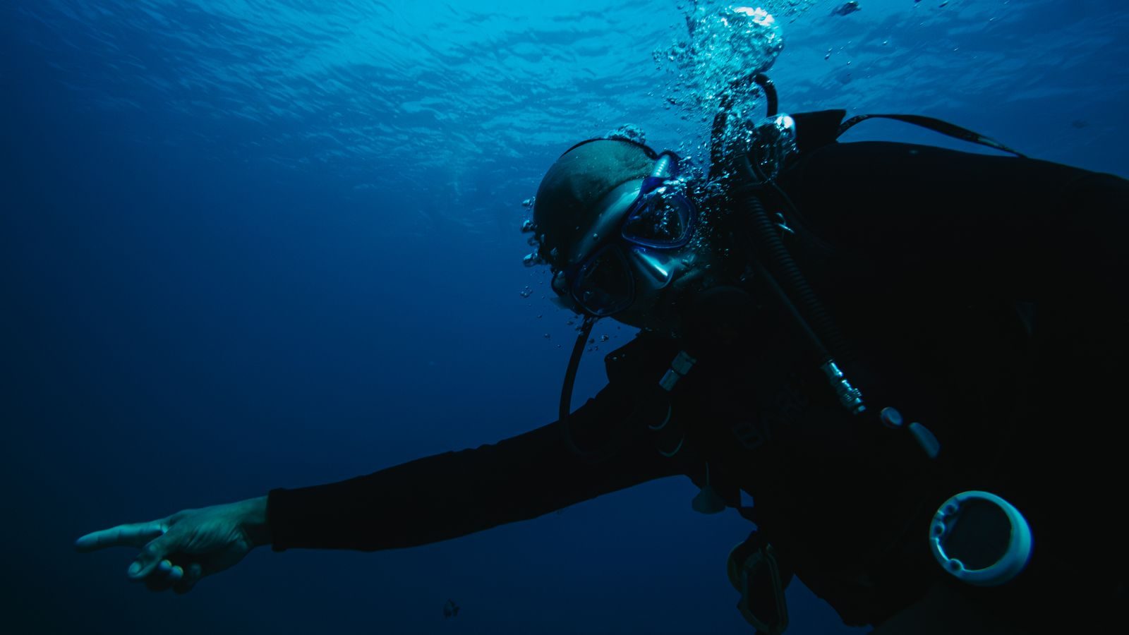 A scuba diver pointing while underwater, surrounded by bubbles.