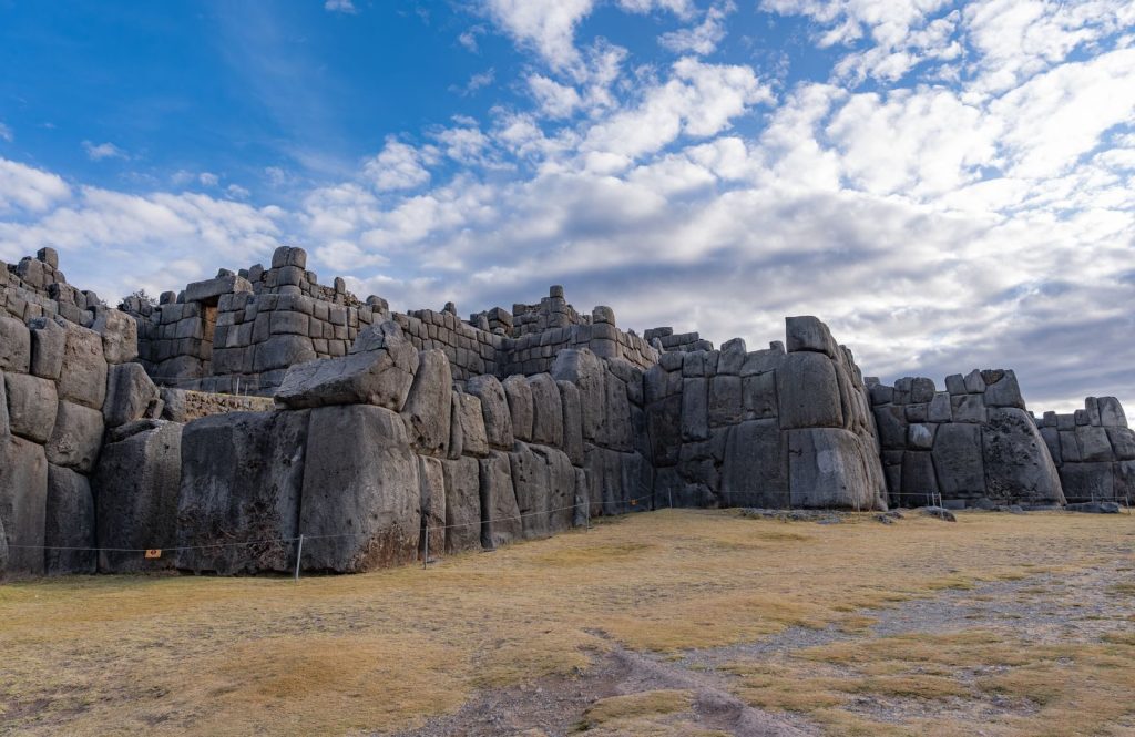Explore the ancient Inca stone walls of Sacsayhuamán under a partly cloudy sky in Cusco, Peru, a marvel of history and architecture.