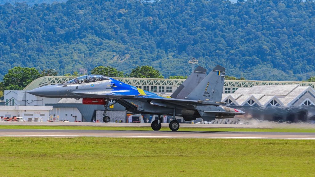 A colorful fighter jet takes off from an airfield against a mountain backdrop, showcasing aviation prowess.