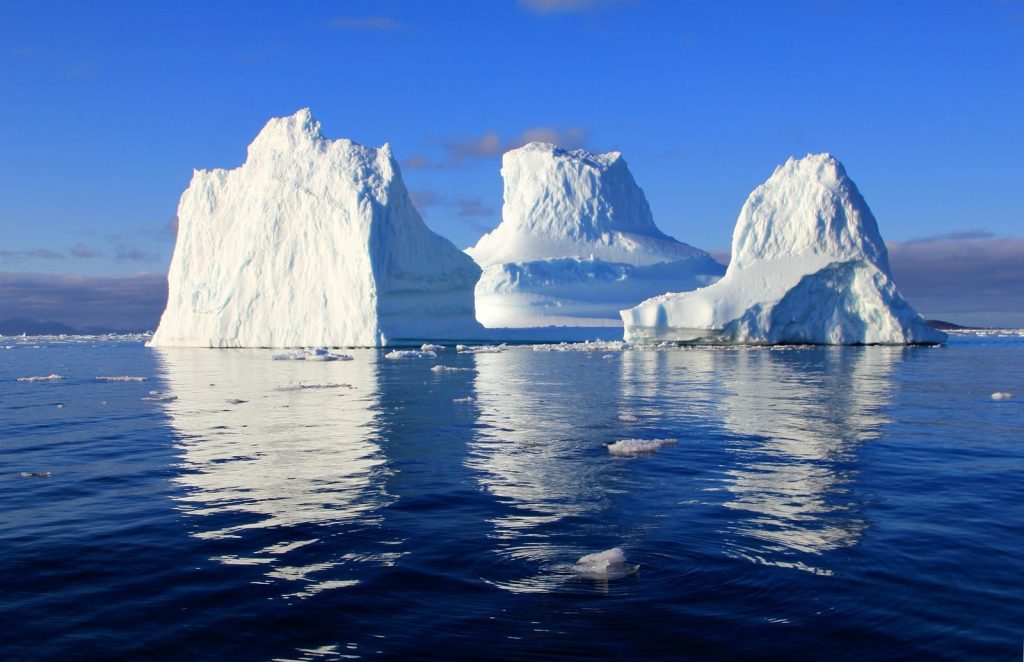 Stunning view of massive icebergs reflecting in serene ocean under a bright blue sky.