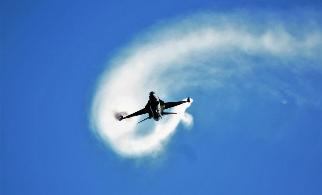 Dynamic shot of a fighter jet soaring through the blue sky, leaving a vapor trail in its wake.