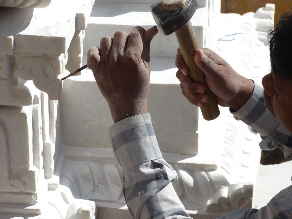 Close-up of an artisan crafting an intricate stone sculpture using hammer and chisel.