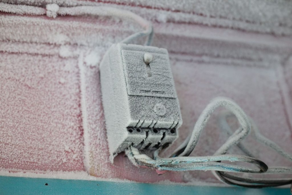 An electrical switch covered in frost and ice during winter on a building's exterior wall.