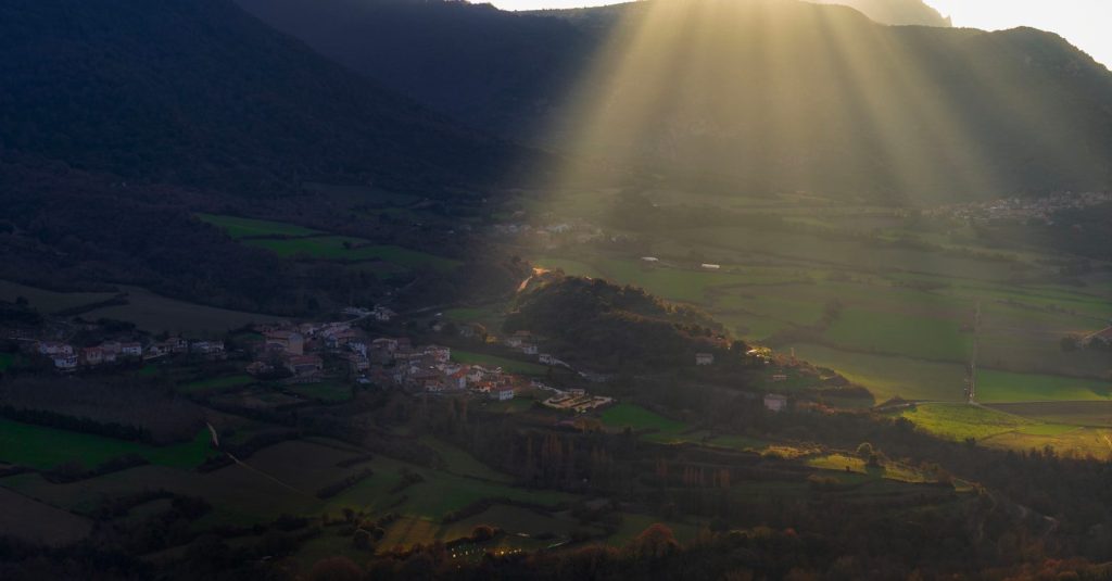 Sunbeams shine on a distant village nestled in hills.