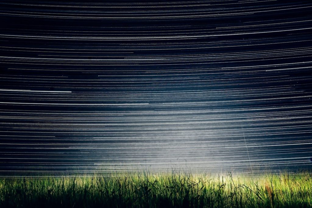 a grassy field with a star trail in the sky