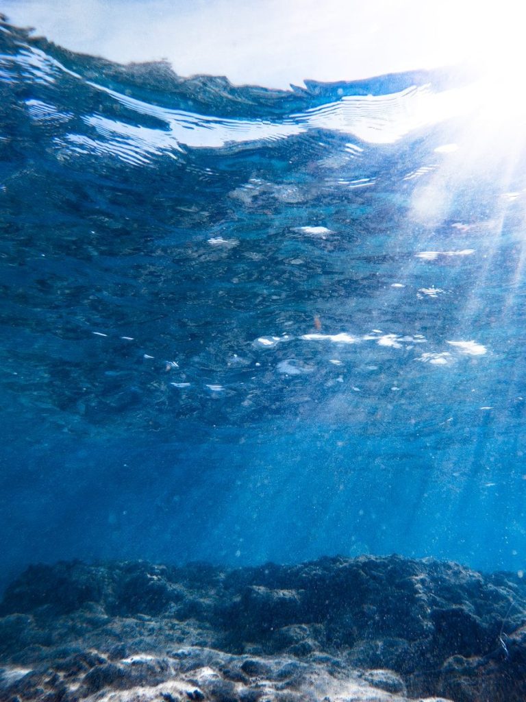 Sunlight streams through ocean surface onto rocky seabed.