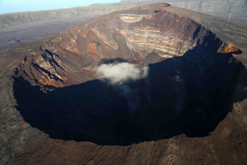 Stunning aerial view of a volcanic crater with smoke and rugged terrain under a clear sky.