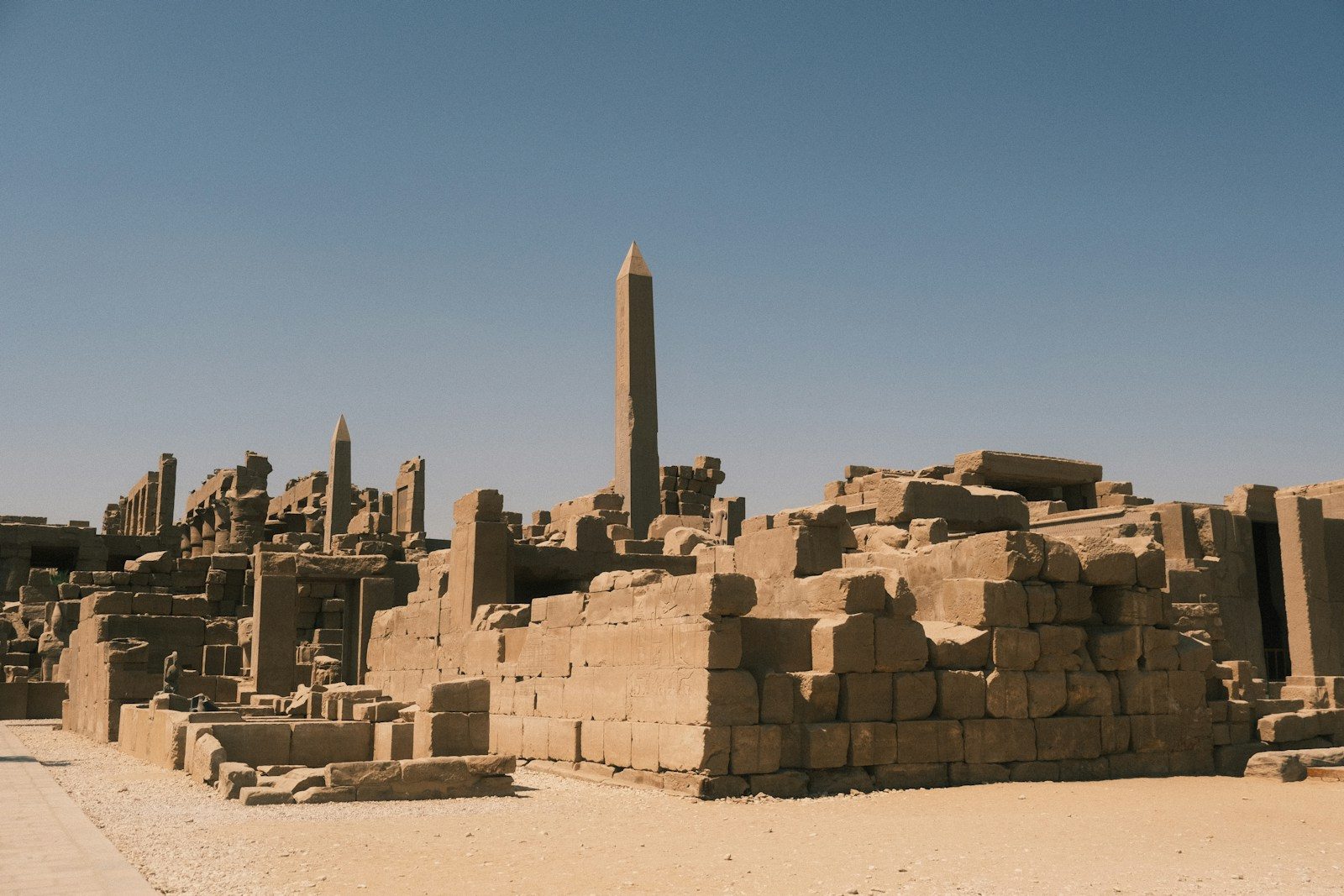 Ancient egyptian ruins with a tall obelisk under clear sky.