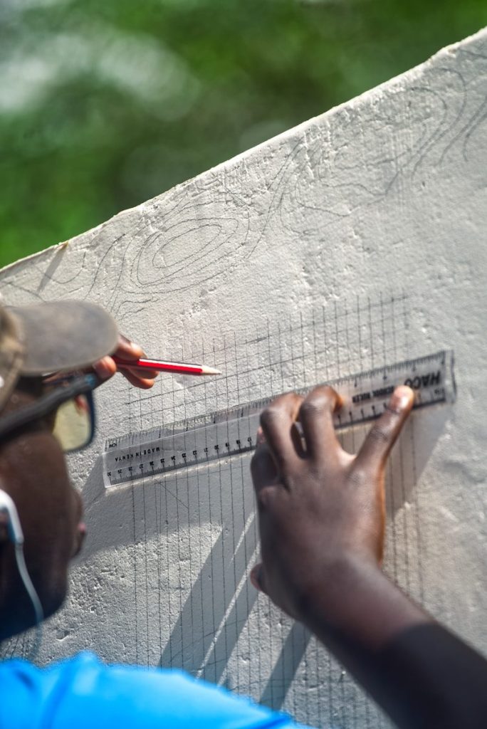Person drawing grid lines on concrete with ruler.
