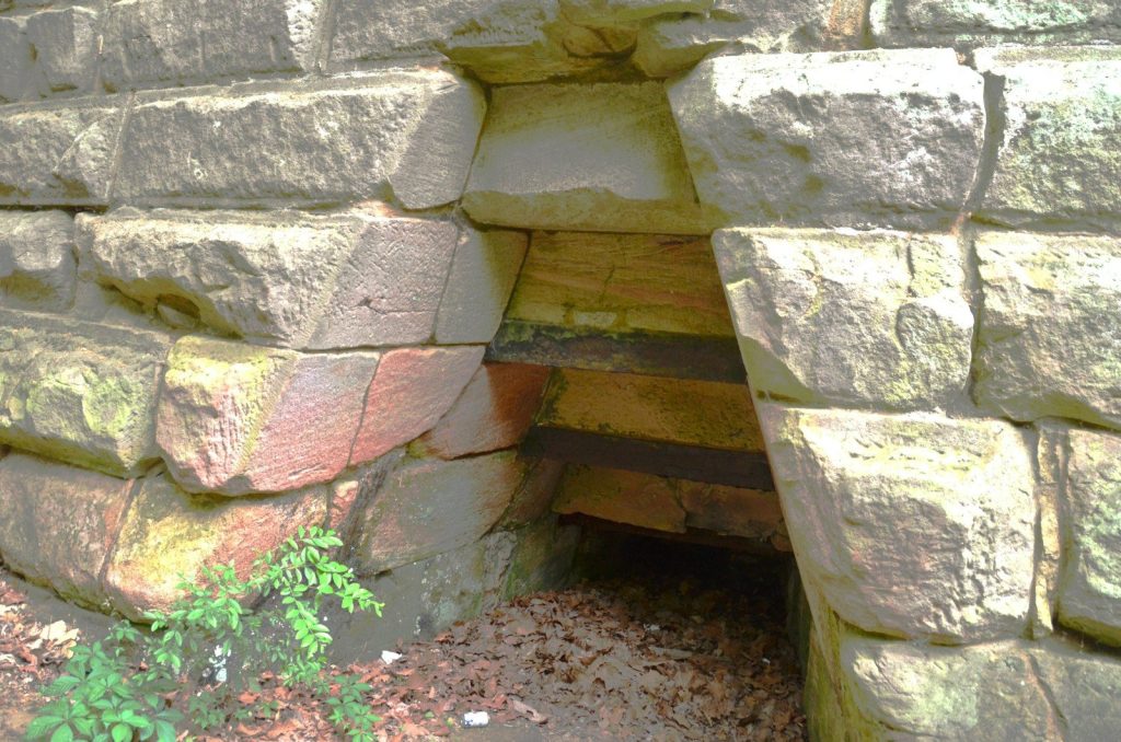 Rough stone wall with a dark, triangular opening.