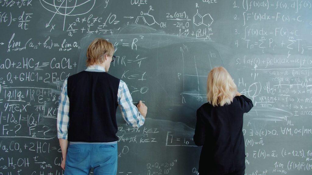 Two students solving math problems on a blackboard.