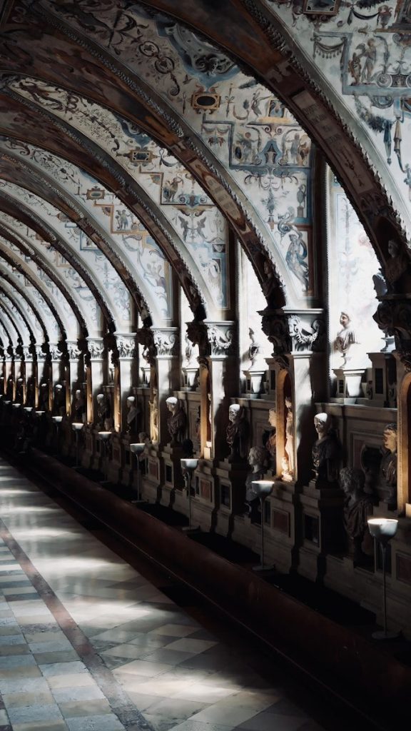 Ornate arched hallway with statues and painted ceilings.