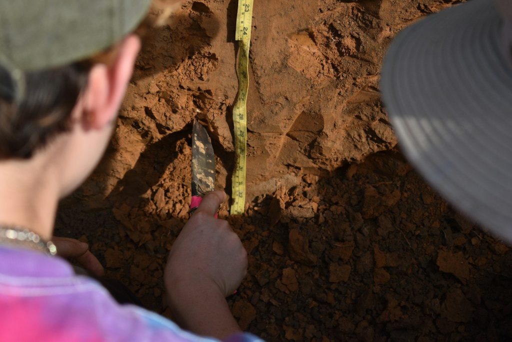 People are examining the soil with a measuring tape.
