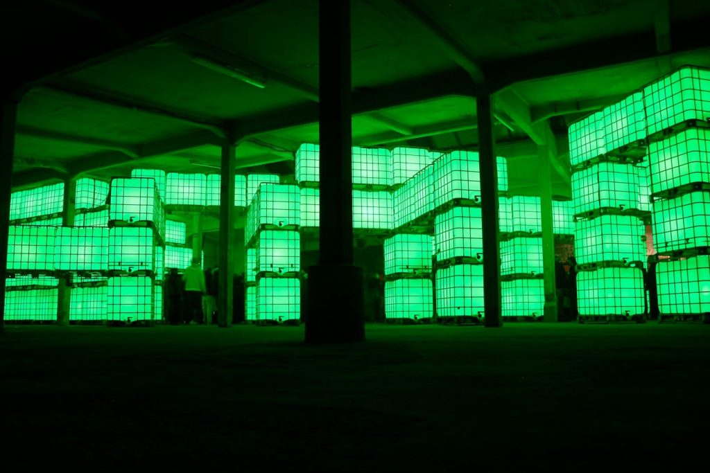 Stacked glowing green containers in a dark industrial space.