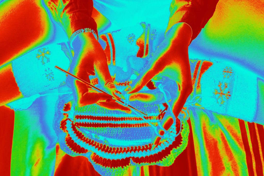 Hands are weaving a colorful patterned basket.