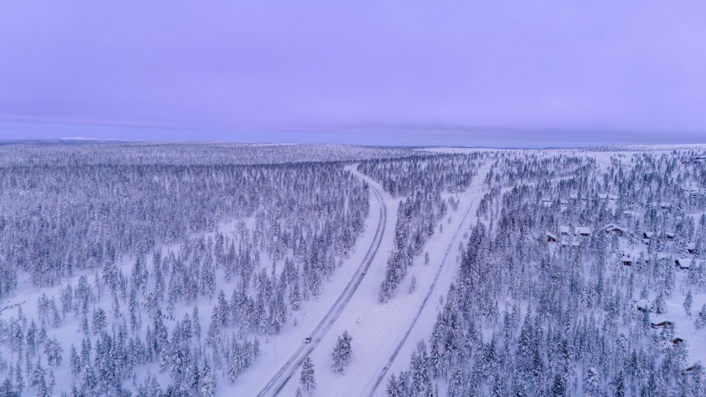 Snowy forest with a winding road under a purple sky.