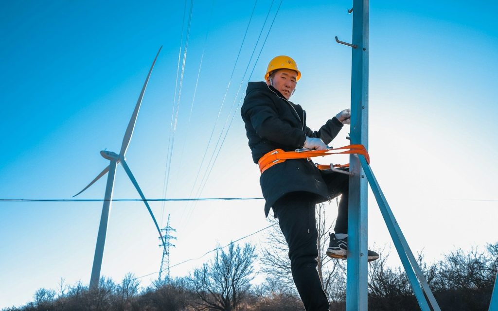 man in black jacket and orange helmet sitting on brown wooden ladder during daytime