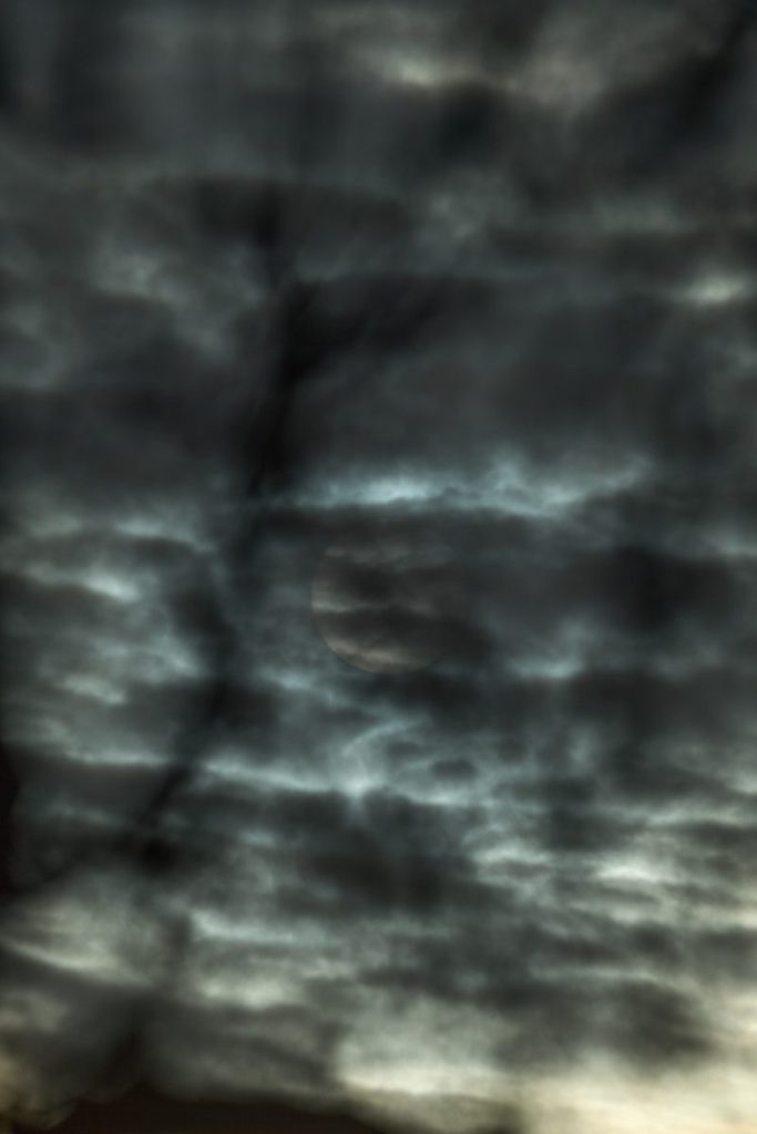 a plane flying through a cloudy sky with the moon in the distance