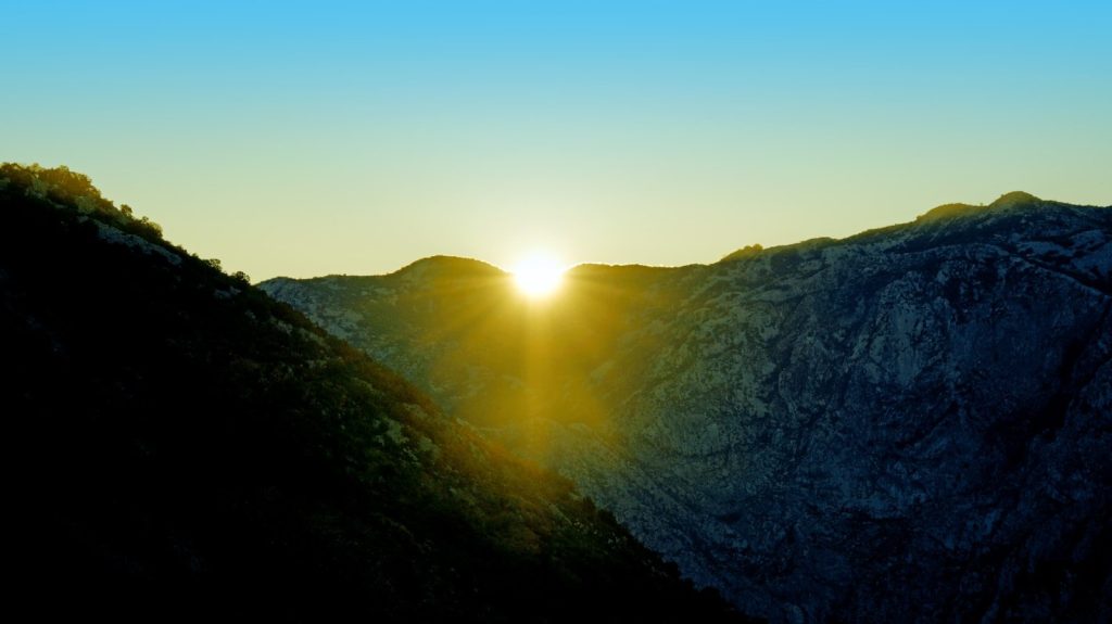 Sunrise over rugged mountains with a bright sunburst.