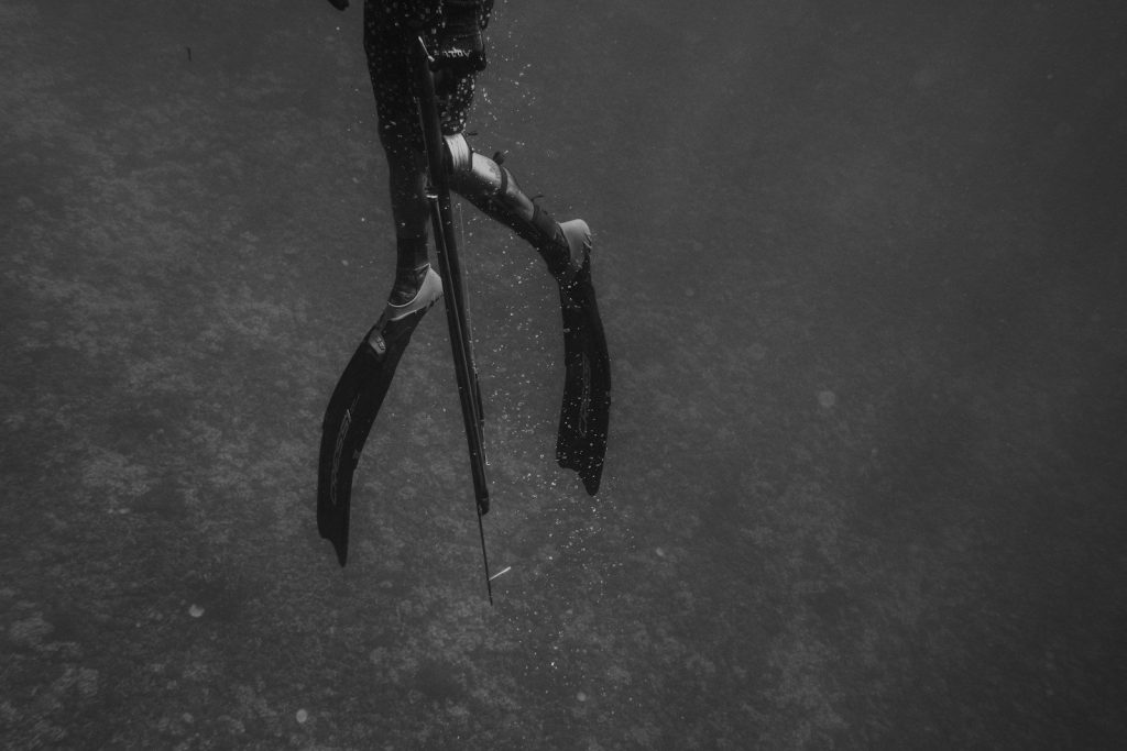grayscale photo of man in black wet suit holding black rifle
