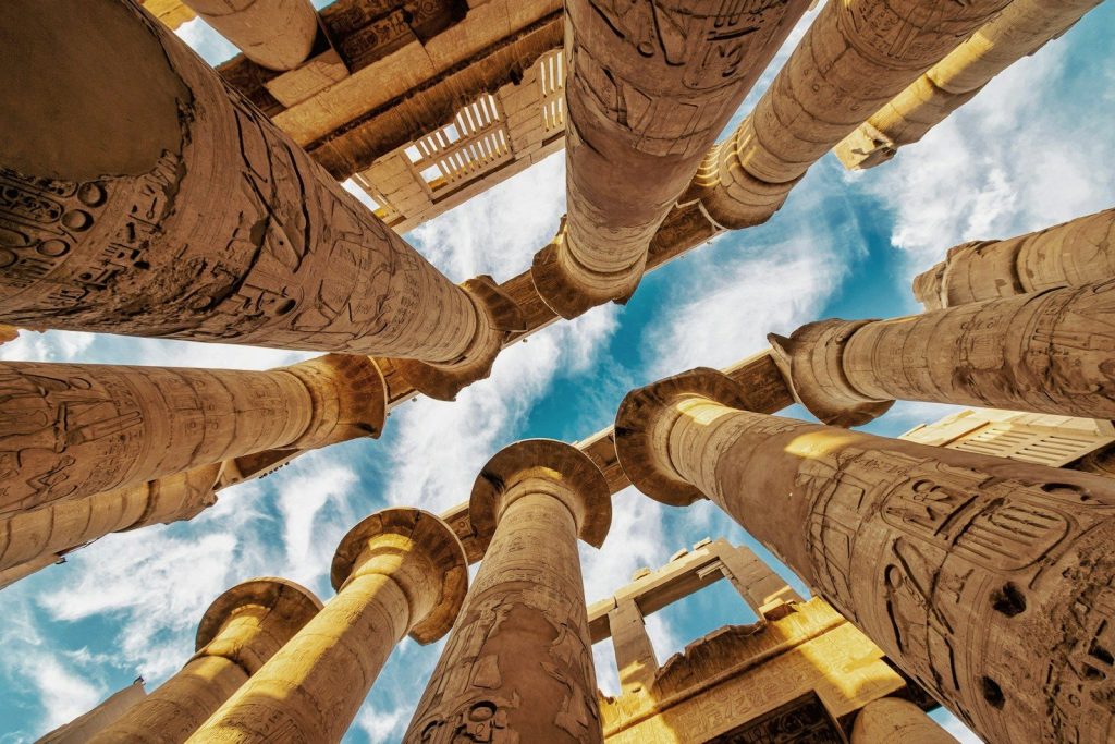 Looking up at ancient egyptian columns against a blue sky.
