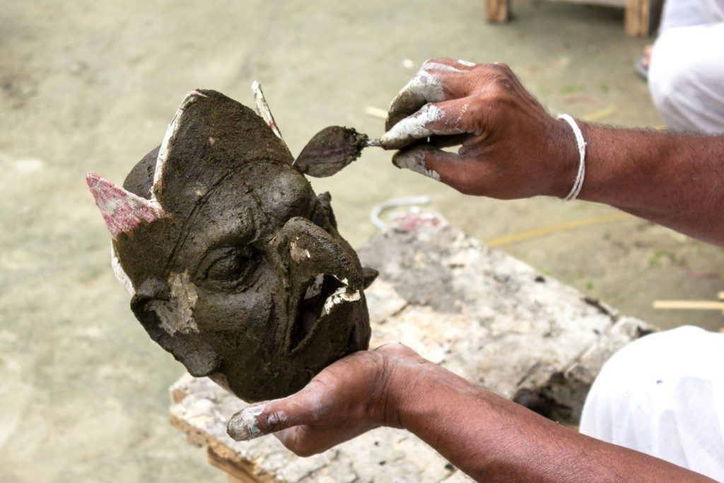 Hands sculpting a clay mask with intricate details.