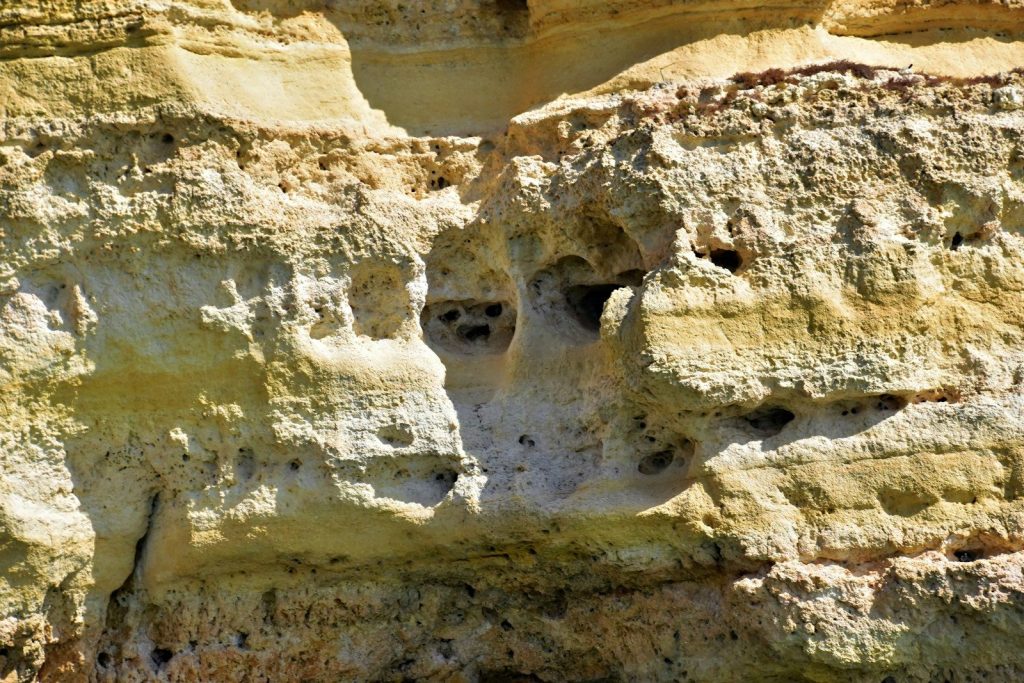Weathered sandstone cliff with natural holes and man-made holes.