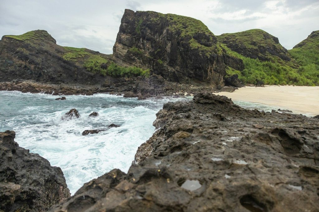 a rocky beach with a large body of water and a large cliff with Kynance Cove in the background