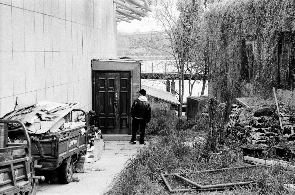 Man stands by a weathered wooden door near a river.