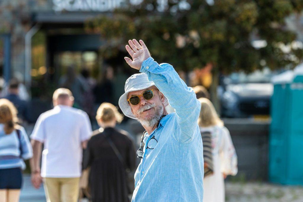 Man in hat and sunglasses waves hello.