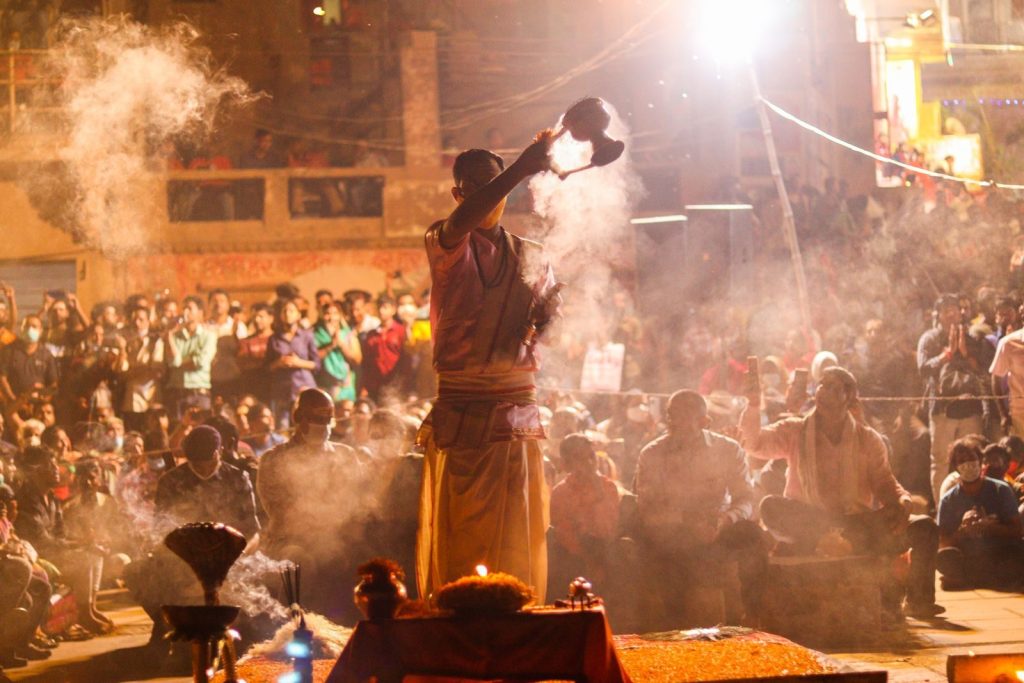 Religious ceremony with incense, smoke, and worshippers gathered under night lights.